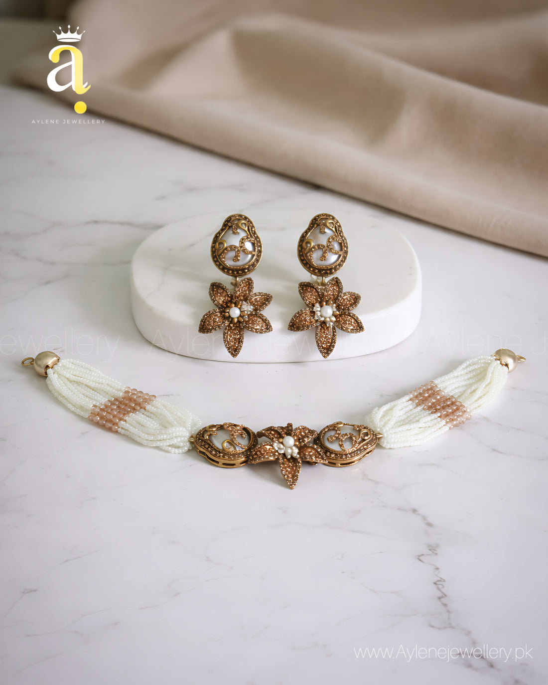 Jewelry set with earrings and a necklace on a marble surface with a beige fabric background.